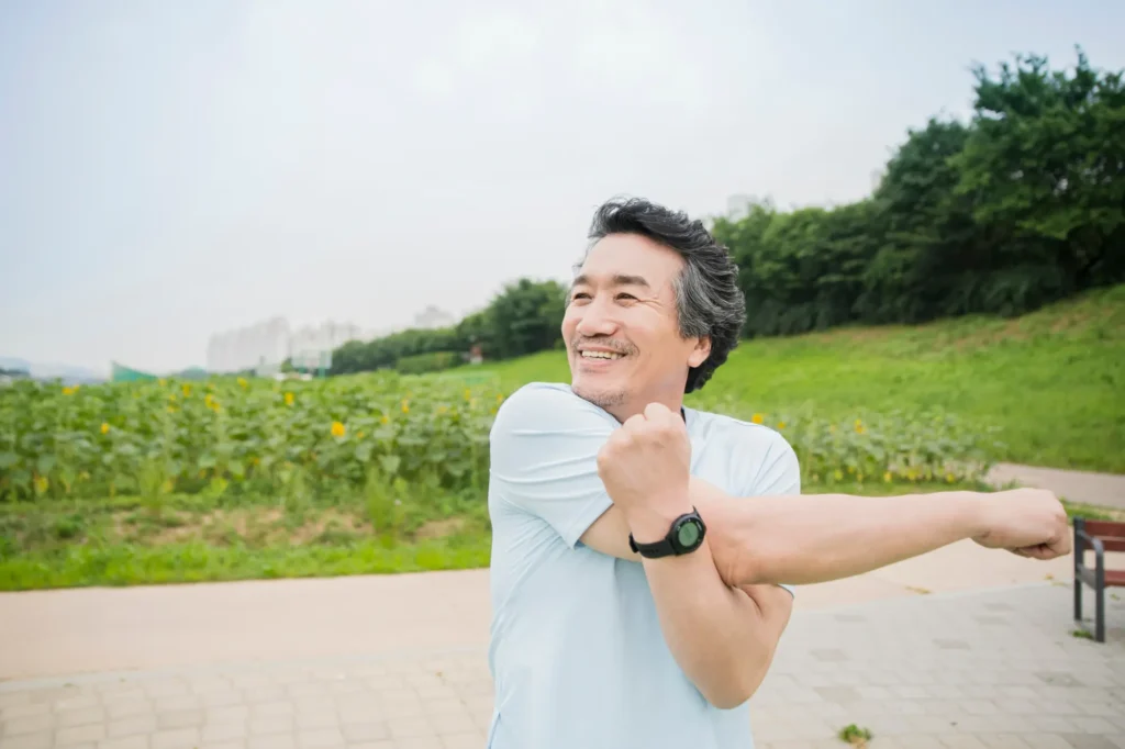 A middle aged man doing a cross body stretch hoping to prevent shoulder arthritis